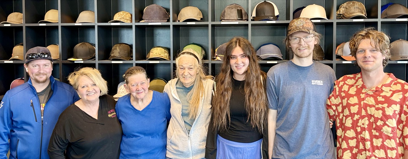 The Pine Needle Embroidery crew in front of the hat wall